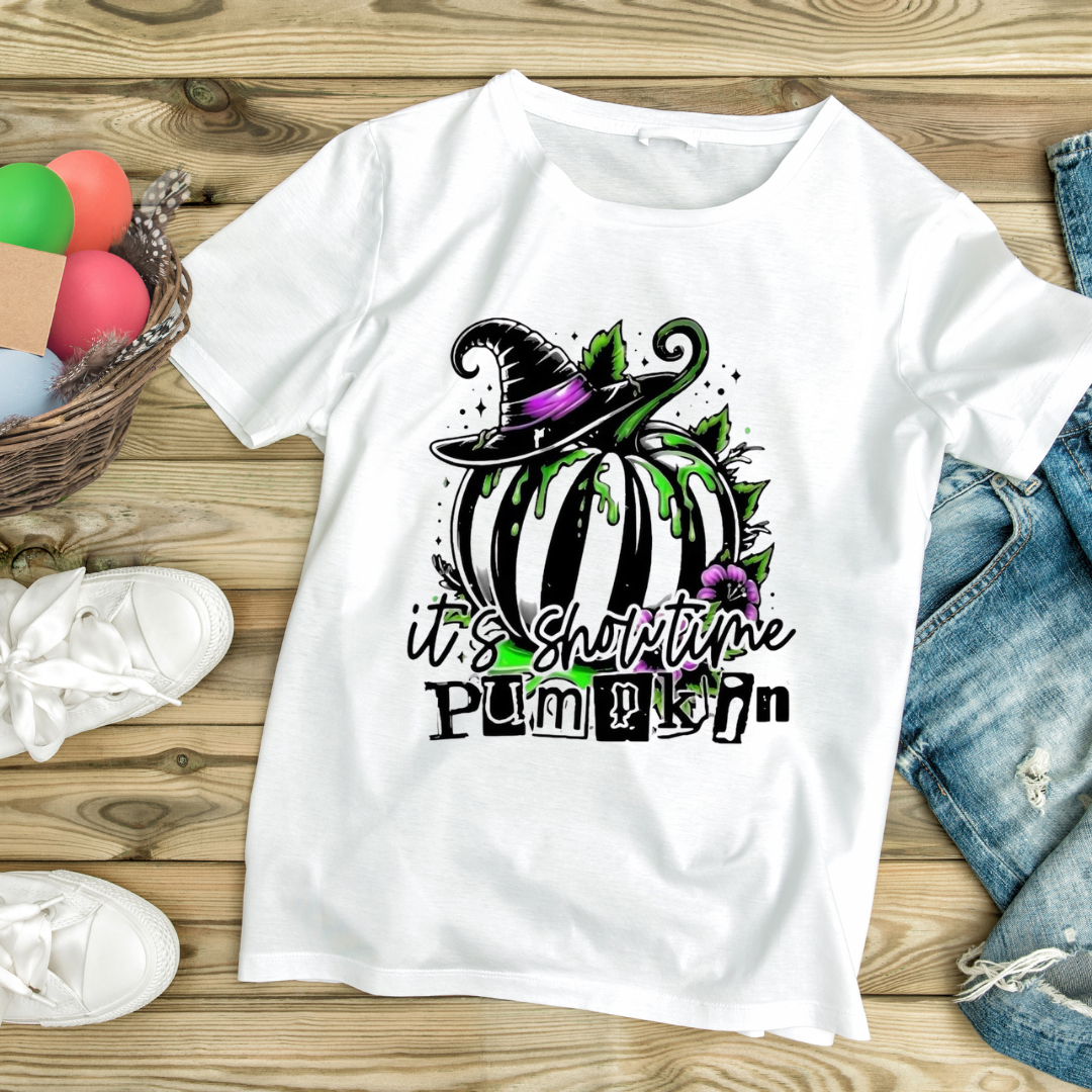 White t-shirt featuring It's Showtime pumpkin design with a witch hat and green details