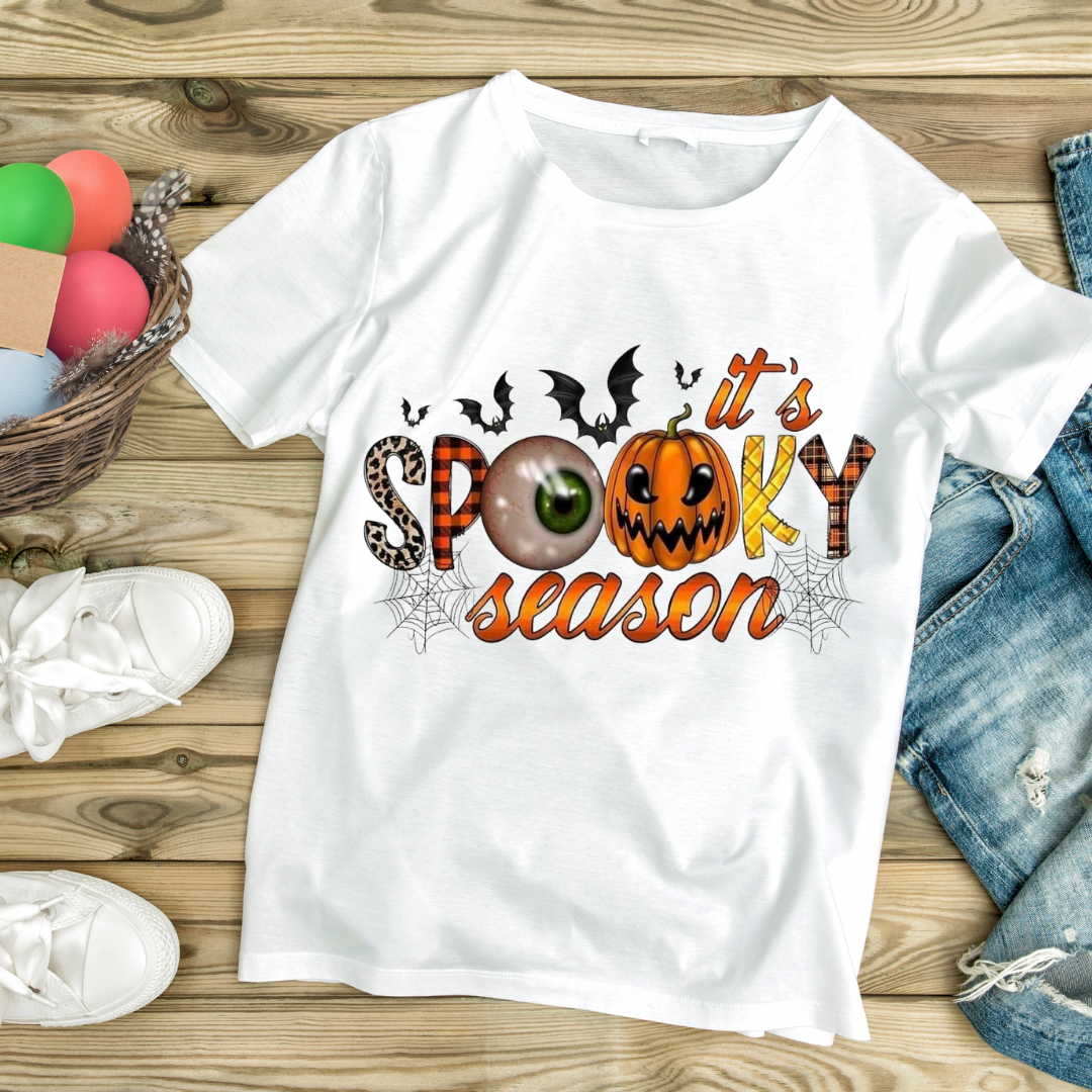 Halloween graphic tee with spooky season design featuring pumpkin, eyeball, bats, and spider webs