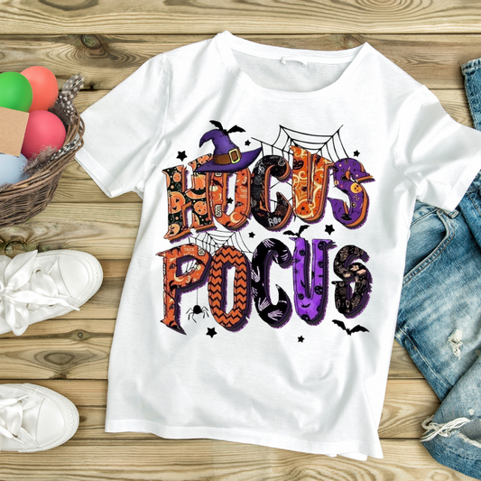 White Hocus Pocus themed shirt with colorful Halloween letters and designs laid flat on wooden floor
