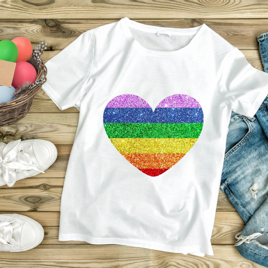 White t-shirt with a glittery rainbow-striped heart design laid on wooden surface with denim shorts and white sneakers